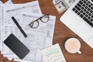 A pair of glasses, a pen, and a cup of coffee sitting on a desk with tax forms.