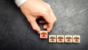 A hand placing a tile with the image of a storefront in line with other tiles with storefronts.